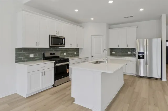 a kitchen with stainless steel appliances white cabinets a sink a stove a refrigerator and white cabinets