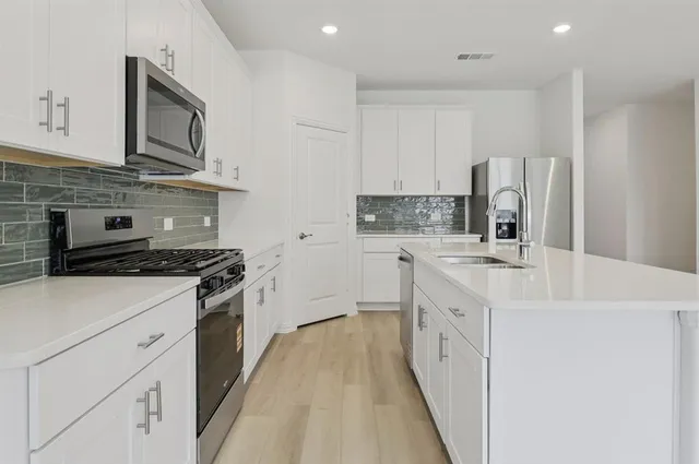 a kitchen with stainless steel appliances granite countertop white cabinets a sink a stove a refrigerator and white cabinets