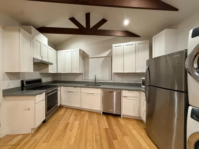 a kitchen with stainless steel appliances a refrigerator a sink and white cabinets