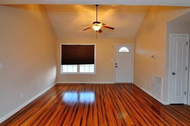 a view of a room with wooden floor a ceiling fan and window