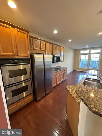 a kitchen with stainless steel appliances granite countertop a refrigerator a stove and a sink with wooden floor