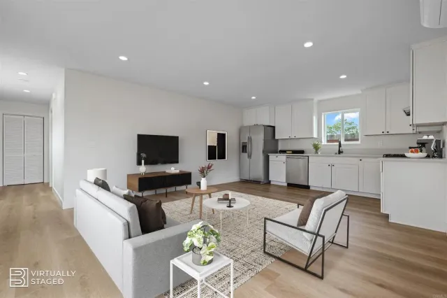 a living room with stainless steel appliances furniture a flat screen tv and a refrigerator