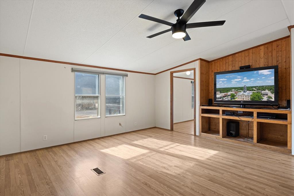 2903 Centaurus Way Granbury, TX 76048 - Photo 7 of 31 Unfurnished living room featuring lofted ceiling, ornamental molding, light wood-type flooring, ceiling fan, and wooden walls