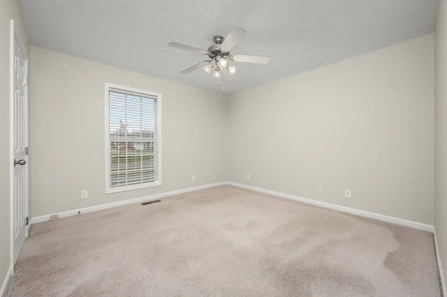 an empty room with chandelier fan and windows