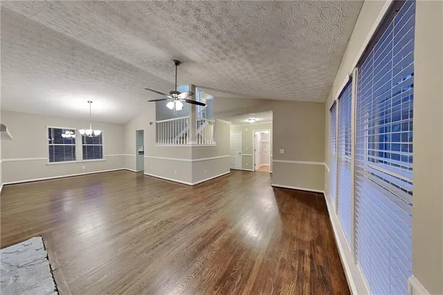 a view of an empty room with wooden floor staircase and a kitchen