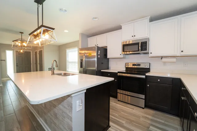 a kitchen with stainless steel appliances kitchen island granite countertop a refrigerator a sink dishwasher a stove and white cabinets with wooden floor