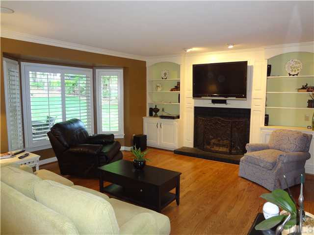 1604 Hunting Ridge Road Raleigh, NC 27615 - Photo 5 of 25 Another View Of The Family Room Showcasing The Beautiful Bay Windows With Pantation Shutters, Hardwood Floors, Golf Course View, and FIreplace. Arch Bookshelves Highlight This Relaxing Room. Den/Family/Great Room