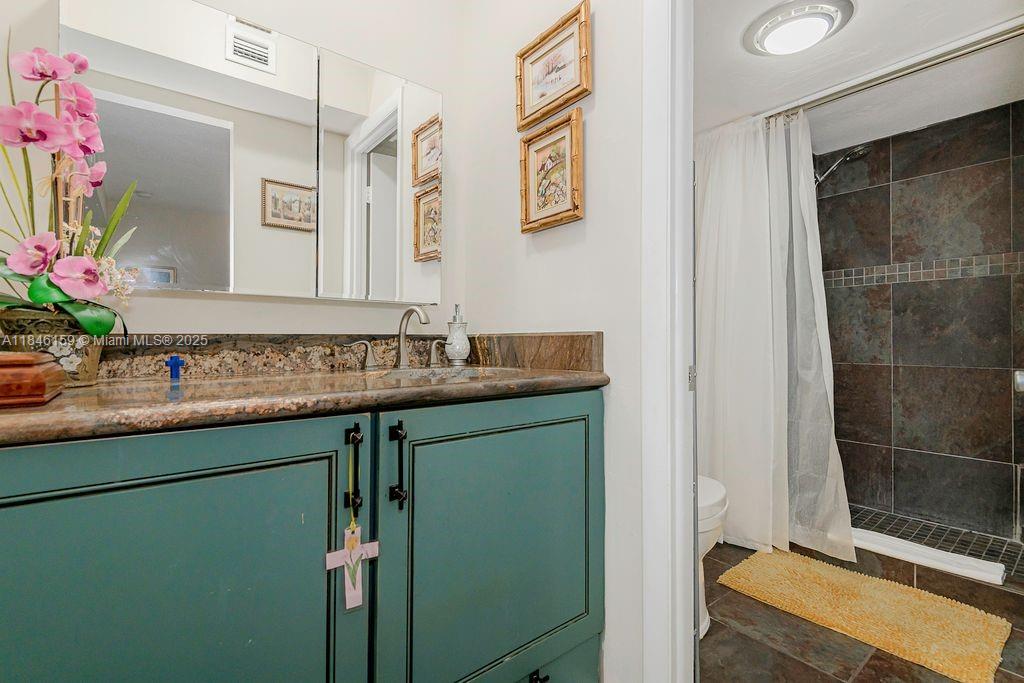 8401 Southwest 107th Avenue, Unit 214E Miami, FL 33173 - Photo 19 of 28 a bathroom with a granite countertop sink a mirror and a shower