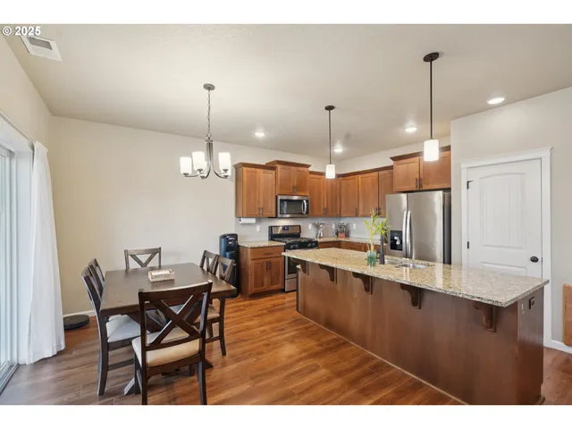 a kitchen with stainless steel appliances kitchen island granite countertop a table chairs and a wooden floor