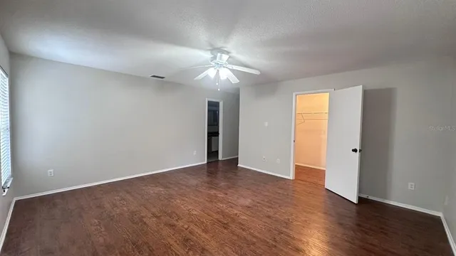an empty room with wooden floor chandelier fan and windows