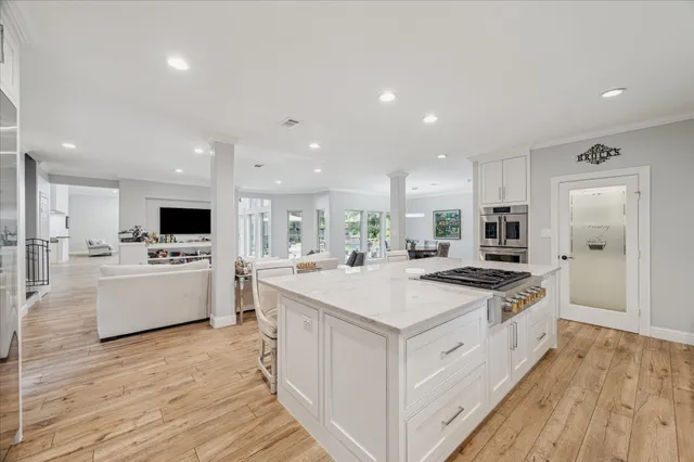 a large white kitchen with a large island oven a stove and a wooden floors