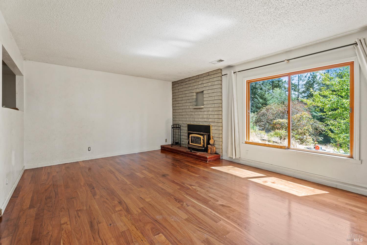 3781 Ridgewood Road Willits, CA 95490 - Photo 8 of 18 an empty room with wooden floor fireplace and windows