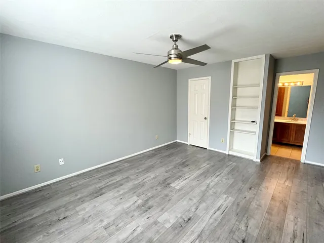 an empty room with wooden floor closet ceiling fan and windows