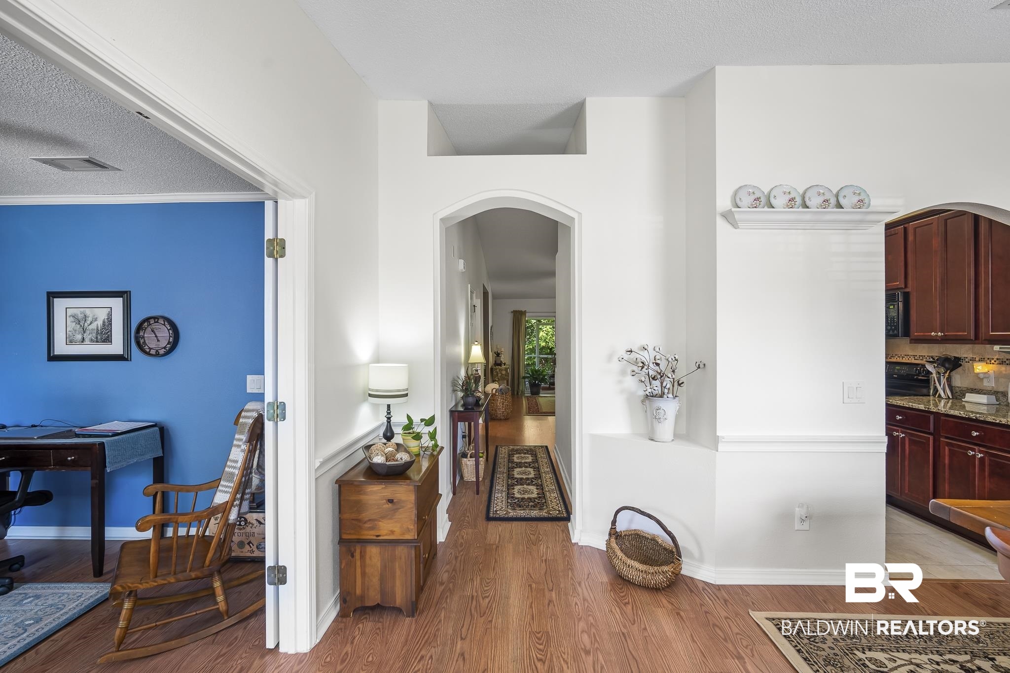Hallway with arched walkways, light wood-style flooring, baseboards, and a textured ceiling