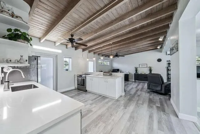 a view of a kitchen with kitchen island stainless steel appliances wooden floors sink and living room view