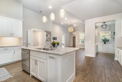 a kitchen with a sink dishwasher a stove and white cabinets with wooden floor