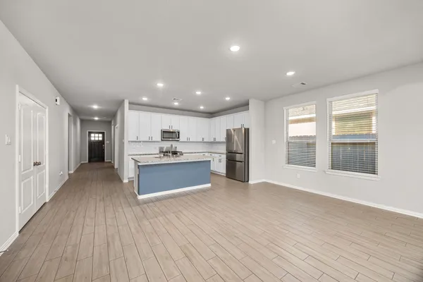 a large kitchen with stainless steel appliances granite countertop a large counter top a wooden floors and a large window
