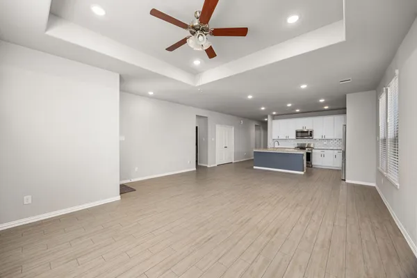 a view of an empty room with kitchen view and wooden floor