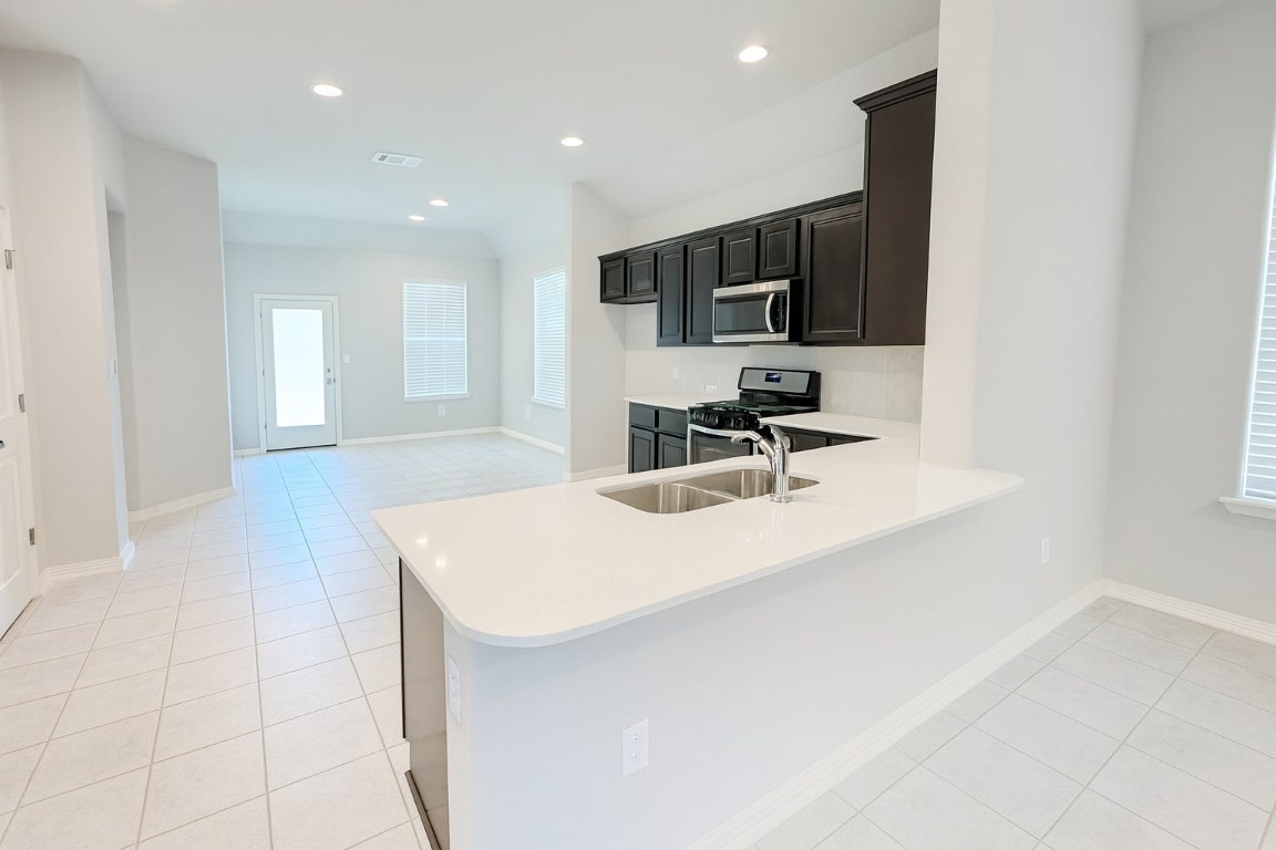 913 Centerra Hills Circle Round Rock, TX 78665 - Photo 4 of 10 Kitchen with dark cabinets, appliances with stainless steel finishes, a peninsula, recessed lighting, and light tile patterned floors