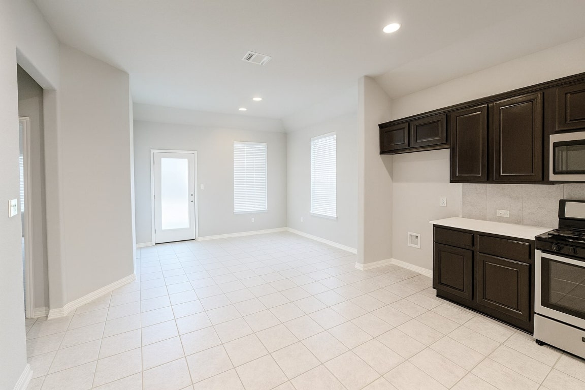913 Centerra Hills Circle Round Rock, TX 78665 - Photo 6 of 10 Kitchen featuring appliances with stainless steel finishes, dark brown cabinetry, light tile patterned flooring, recessed lighting, and decorative backsplash
