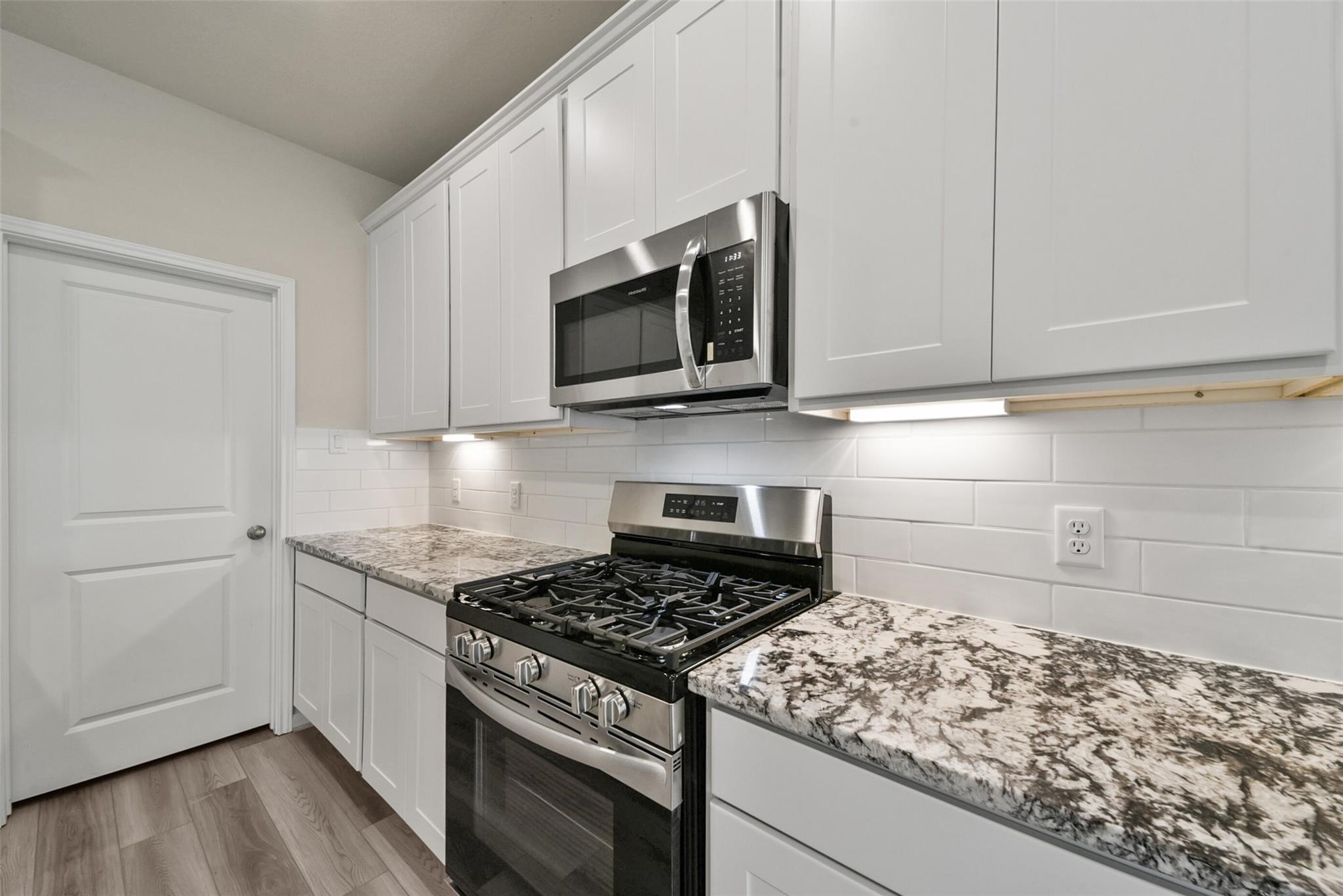 10522 Plumas Run Drive Rosharon, TX 77583 - Photo 9 of 29 Modern kitchen featuring white cabinetry, granite countertops, and stainless appliances with a classic subway tile backsplash.