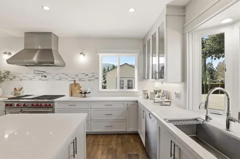 a large kitchen with a refrigerator a sink dishwasher a oven with white cabinets and wooden floor