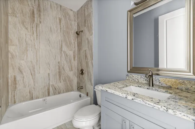 a bathroom with a granite countertop bathtub sink vanity mirror and toilet