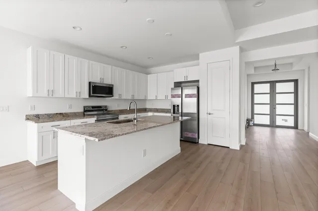 a kitchen with stainless steel appliances granite countertop a stove top oven a sink dishwasher and a refrigerator with wooden floor