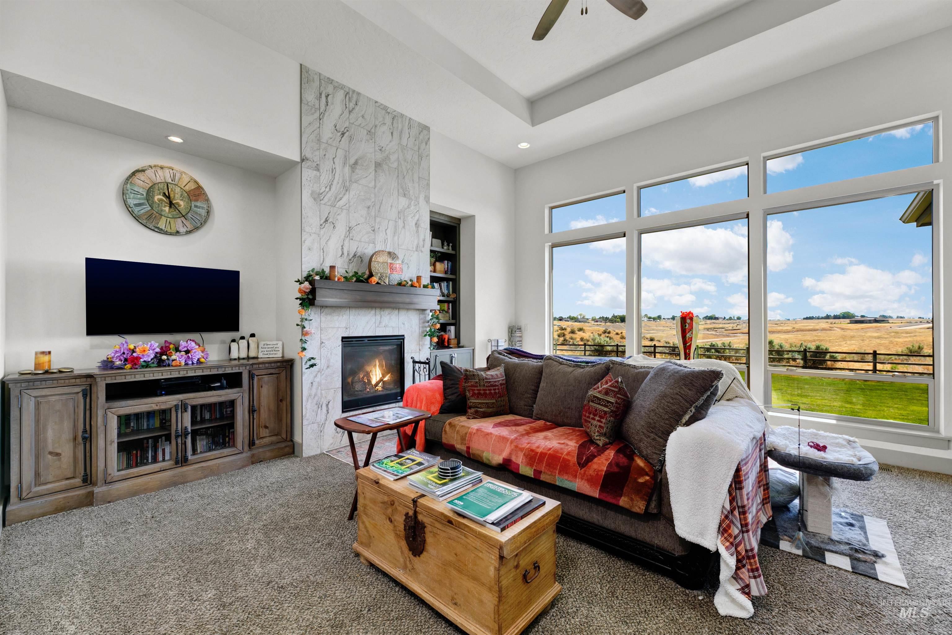 24398 Tombstone Ridge Court Middleton, ID 83644 - Photo 24 of 47 Living area featuring a stone-clad fireplace with a wood mantel, a built-in media console, tray ceiling, and large picture windows showcasing the expansive outdoor landscape