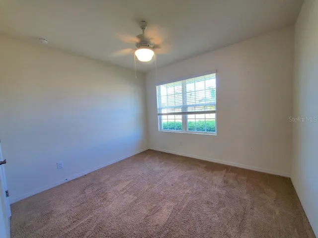 an empty room with a chandelier fan and windows