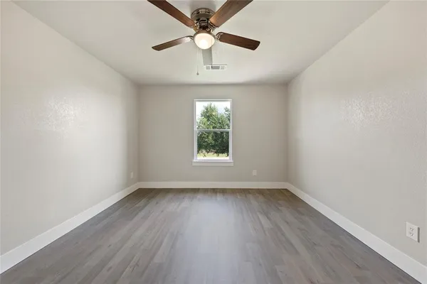 an empty room with wooden floor chandelier fan and windows
