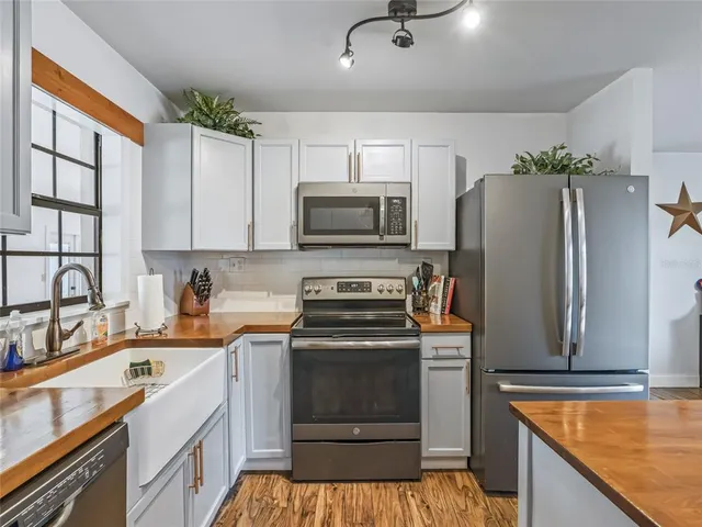 a kitchen with stainless steel appliances kitchen island granite countertop a refrigerator stove and white cabinets with wooden floor