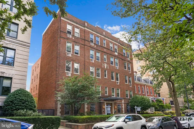 a front view of a building with lot of cars and trees