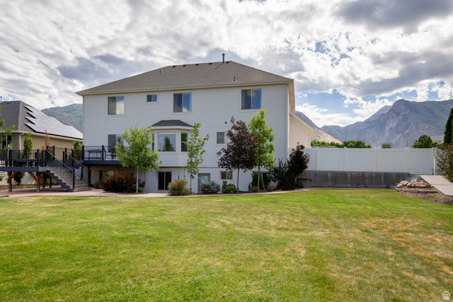868 Braddock Lane Alpine, UT 84004 - Photo 61 of 64 Expansive backyard featuring a manicured lawn, a two-story residence with a bay window, a raised deck with stairs, a white privacy fence, and mountain scenery