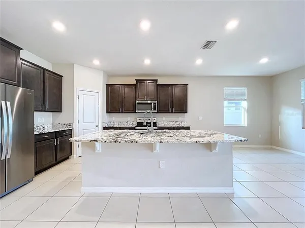 a large kitchen with kitchen island granite countertop a large counter top stainless steel appliances a stove a sink a refrigerator and a window