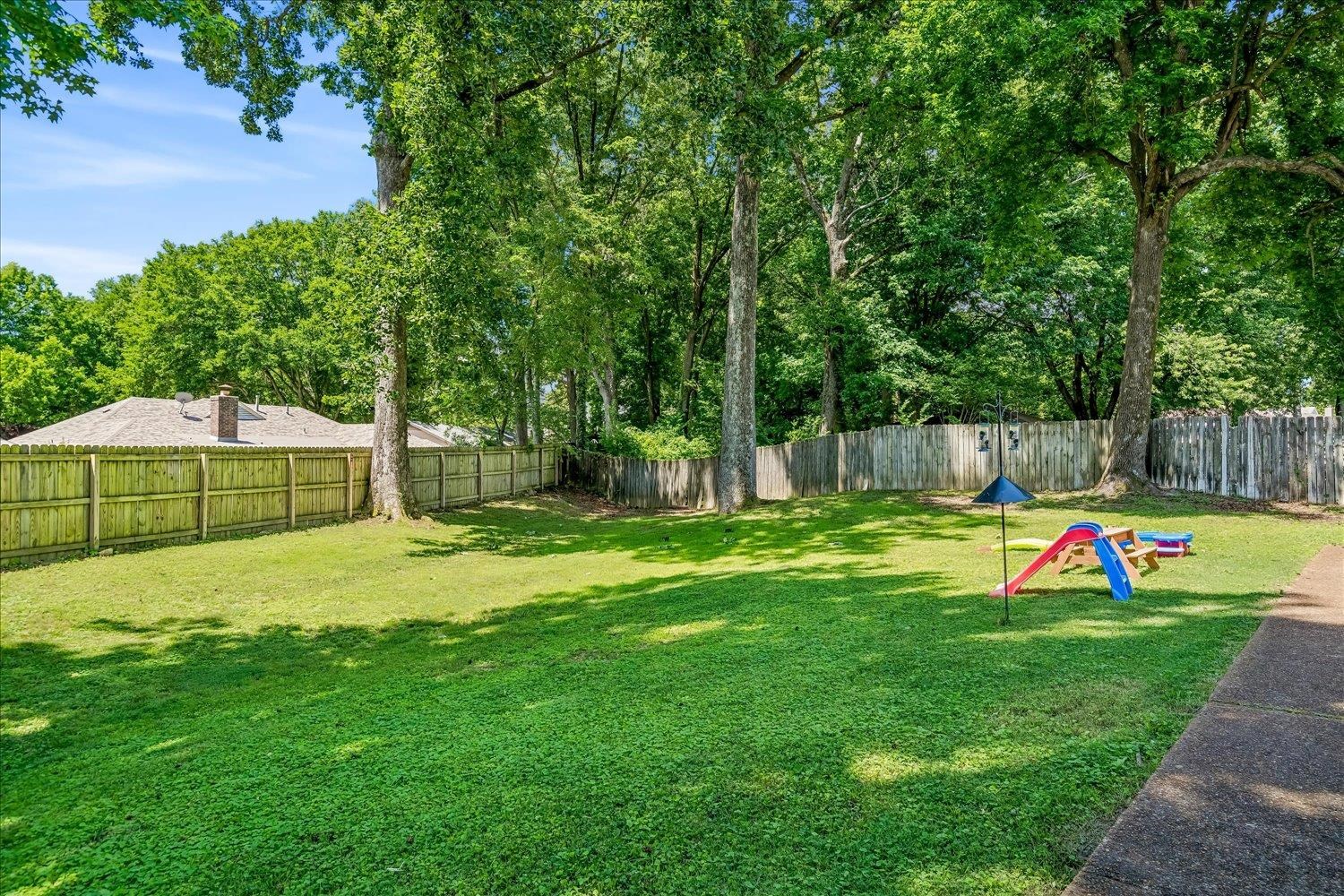 5711 Yale Road Bartlett, TN 38134 - Photo 24 of 29 Expansive backyard featuring a lush green lawn, mature trees providing natural shade, and a full perimeter privacy fence