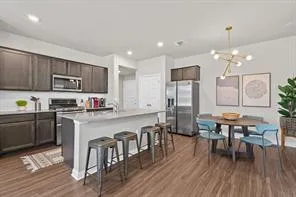 a kitchen with stainless steel appliances granite countertop a refrigerator a stove top oven a sink dishwasher a dining table and chairs with wooden floor