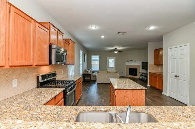 a kitchen with stainless steel appliances granite countertop a stove top oven a sink a dining table and chairs with wooden floor