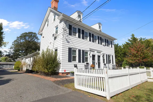 a view of a white house with a small yard and wooden fence