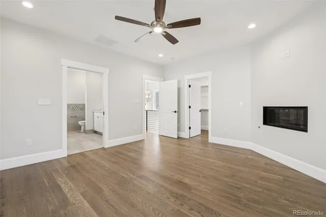 a view of an empty room with wooden floor and a ceiling fan