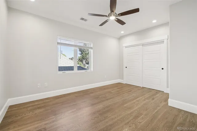 an empty room with wooden floor ceiling fan and windows