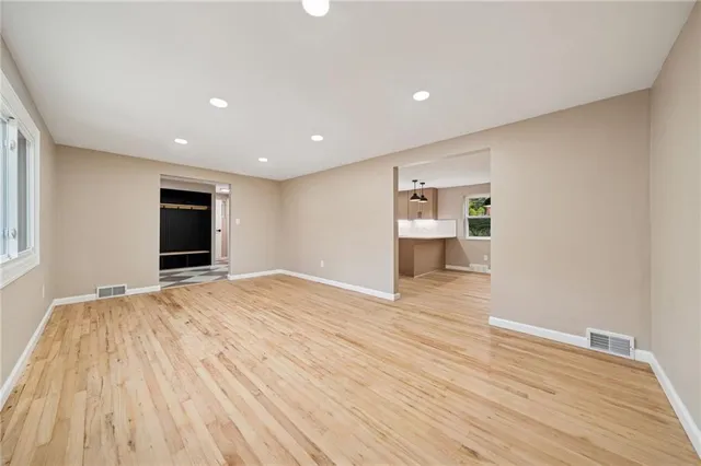 a view of empty room with wooden floor and kitchen