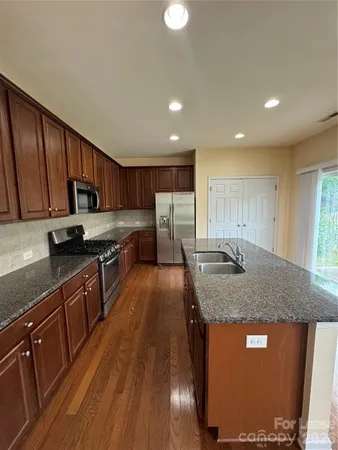a kitchen with stainless steel appliances granite countertop wooden cabinets a refrigerator a sink a stove with wooden floors and wooden cabinets