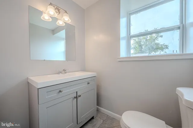 a bathroom with a toilet a sink a mirror a window and vanity