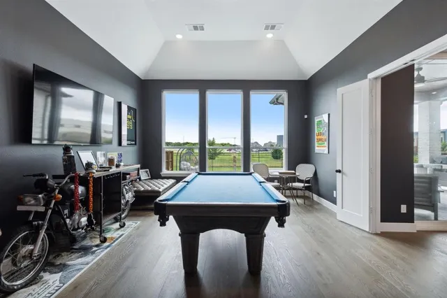 a room with wooden floor pool table and chairs