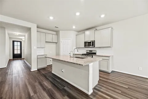 a kitchen with granite countertop a stove top oven a sink dishwasher and a refrigerator with wooden floor
