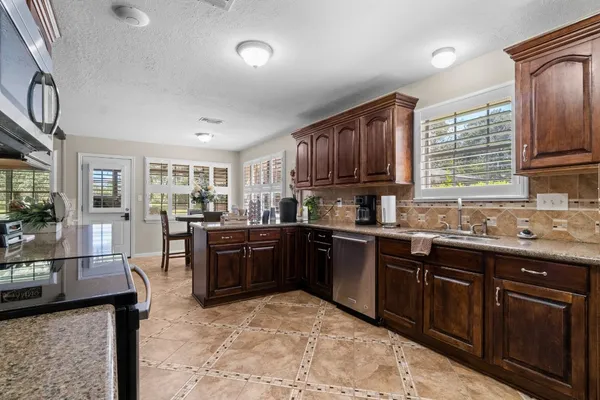 a kitchen with stainless steel appliances granite countertop a stove top oven a sink dishwasher a dining table and chairs with wooden floor