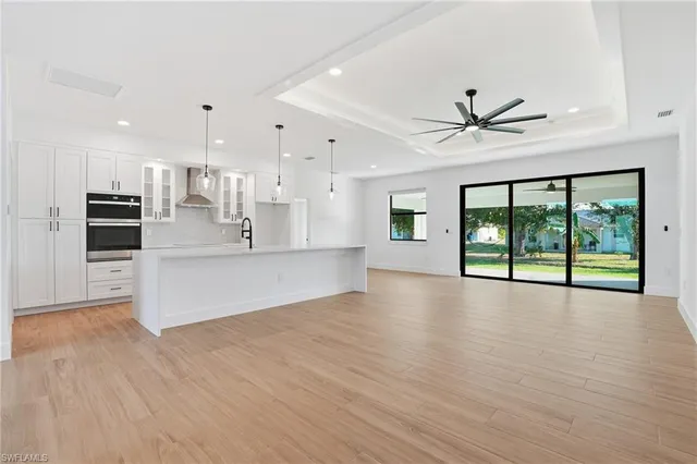 a view of an empty room with kitchen view and wooden floor