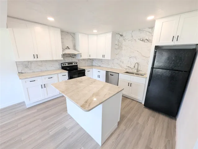 a kitchen with stainless steel appliances granite countertop a refrigerator a sink dishwasher a stove and white countertops with wooden floor