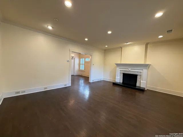 an empty room with wooden floor fireplace and windows